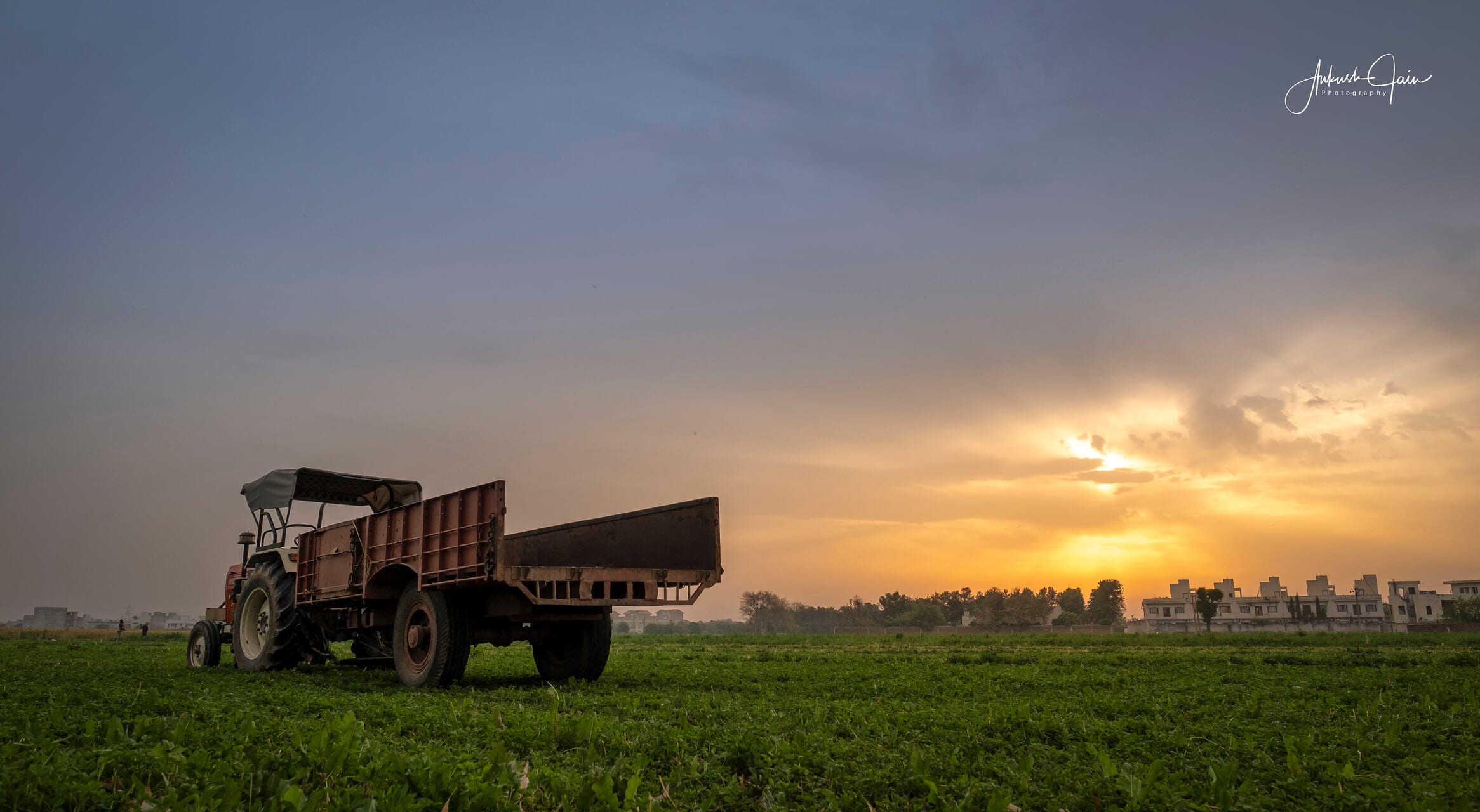Tractor and trailer parked on a green field at sunset, village Issewal
