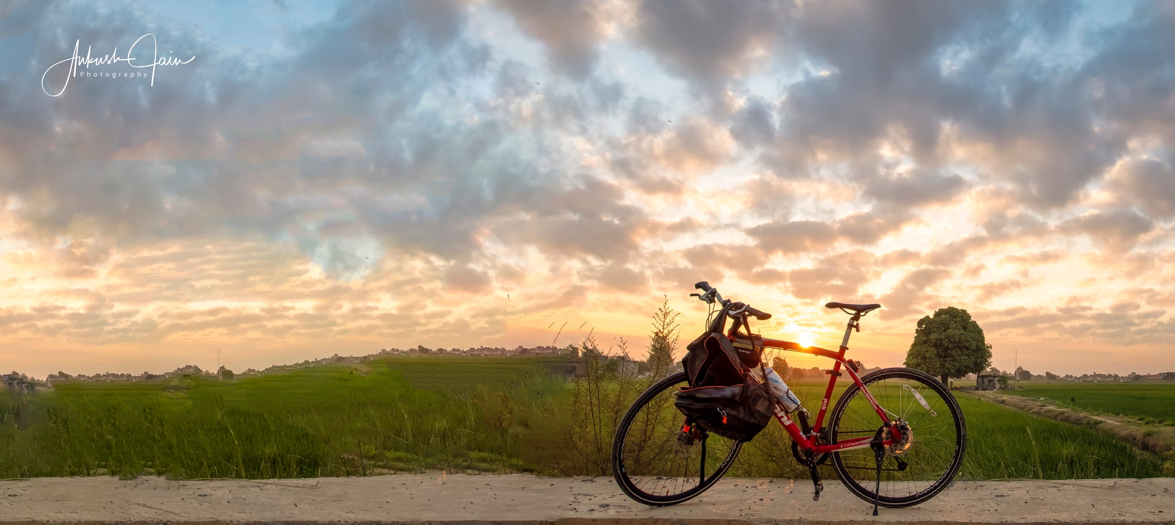 Touring bicycle leant against a roadside wall at sunrise, open fields near Jainpur