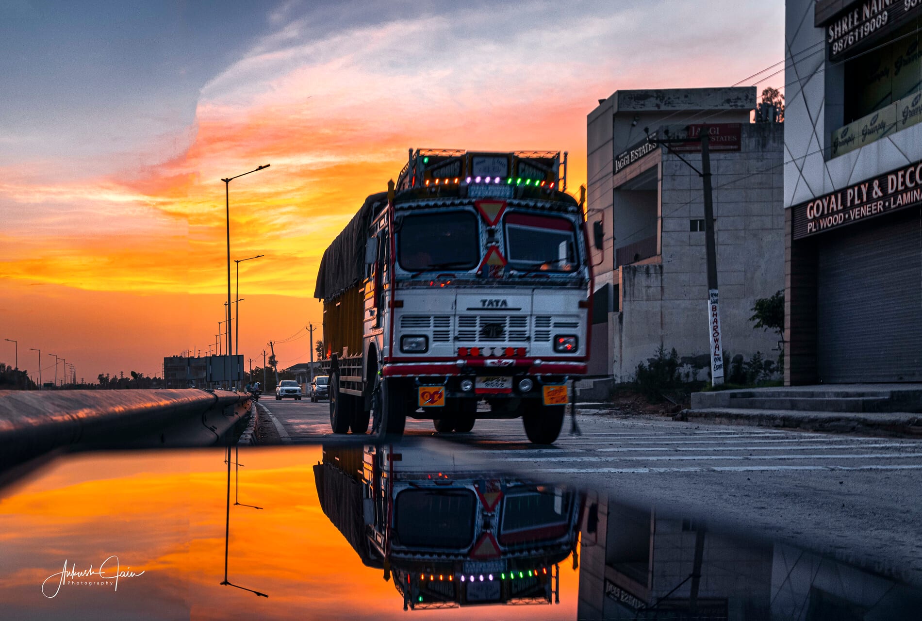 Painted Tata truck on a wet road reflecting an orange sunset, by the canal in South City Ludhiana