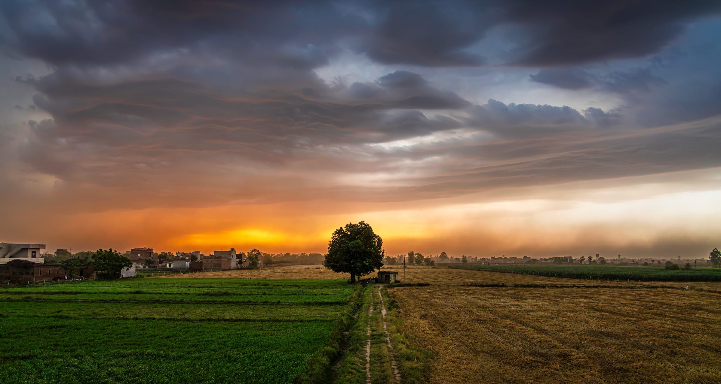 Storm clouds rolling over a green field at sunrise near Jainpur