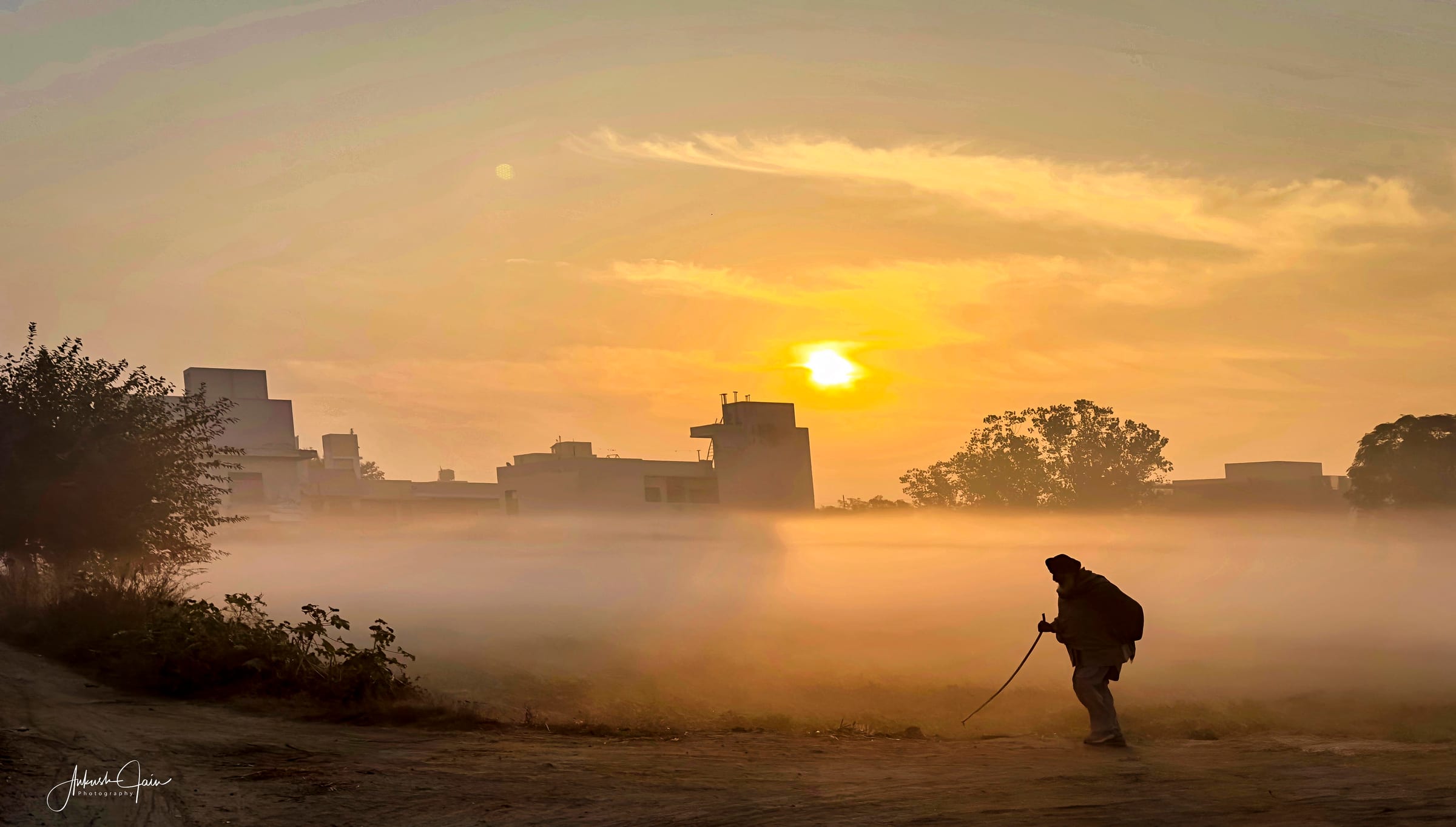 Elderly man walking across a foggy field at sunrise, village Barewal