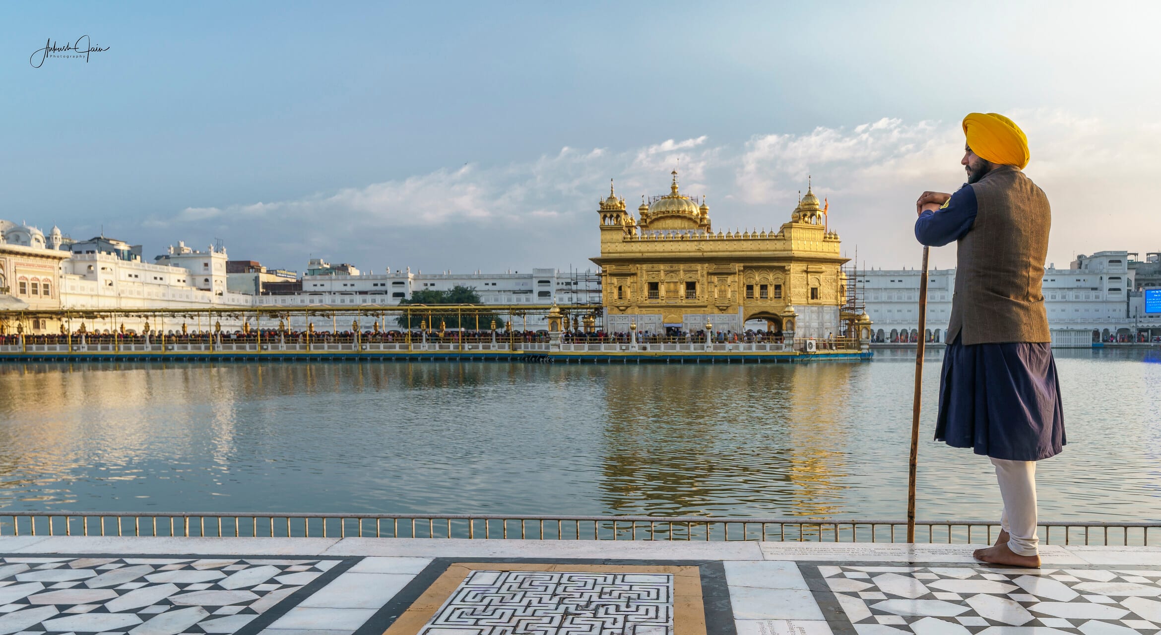 Sikh sevadar with a staff gazing at Harmandir Sahib from the marble parikrama