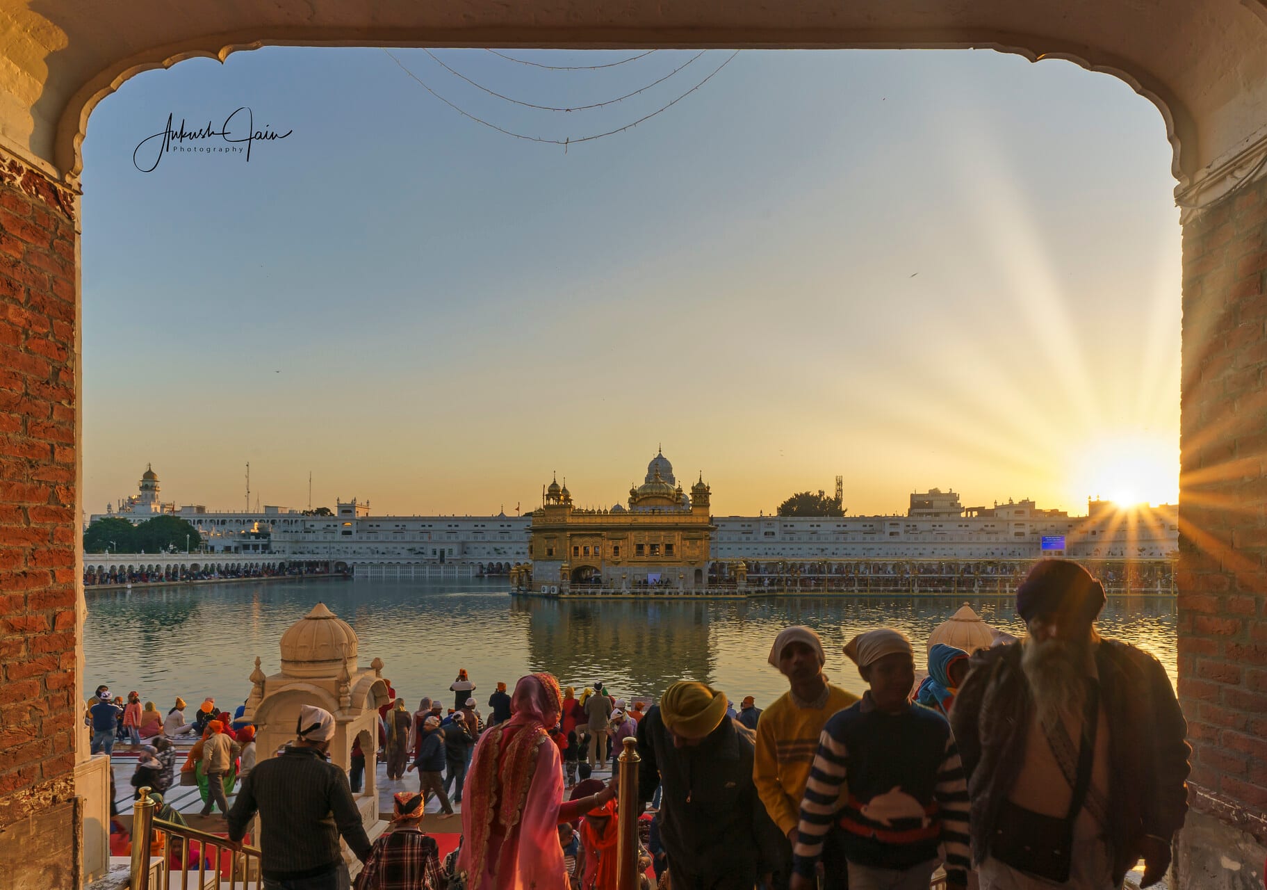 Sun starburst and crowd silhouettes seen through the Darshani Deori arch