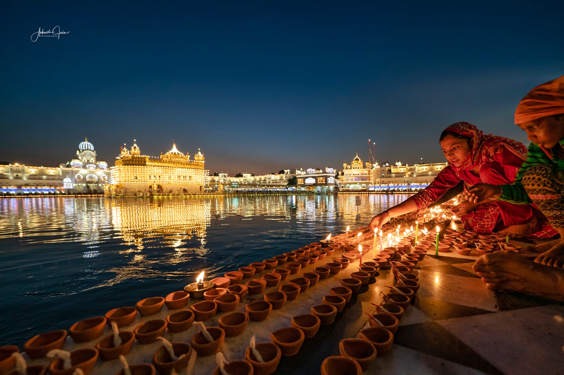 Women lighting rows of diyas at the sarovar edge on Guru Nanak Parkash Utsav