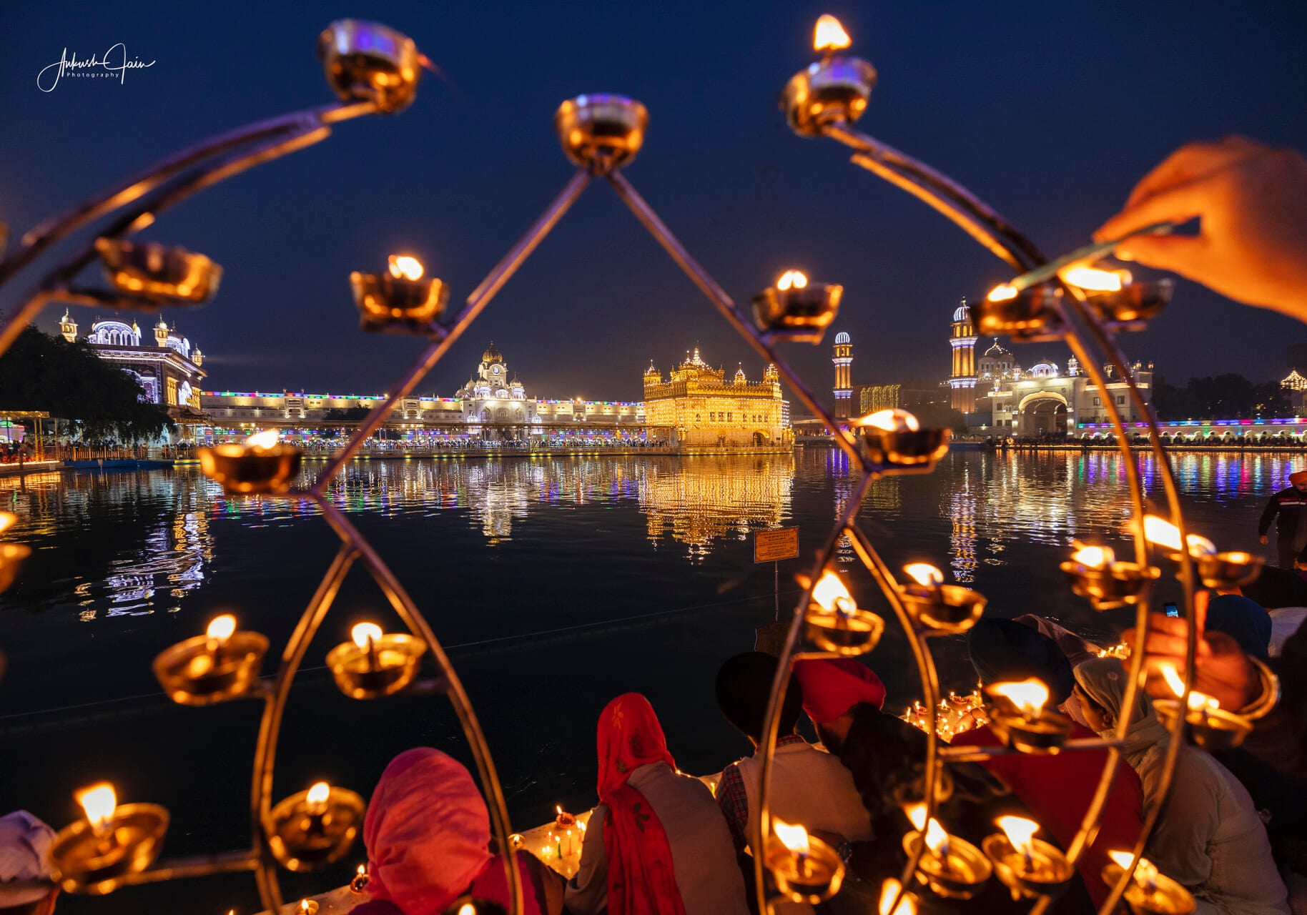 Ornamental diya candelabra at the sarovar edge on Gurpurab, lit temple beyond