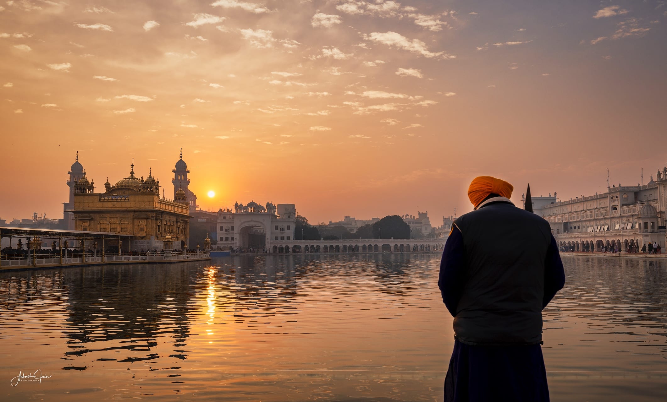 Sevadar in saffron turban watching dawn break over Harmandir Sahib