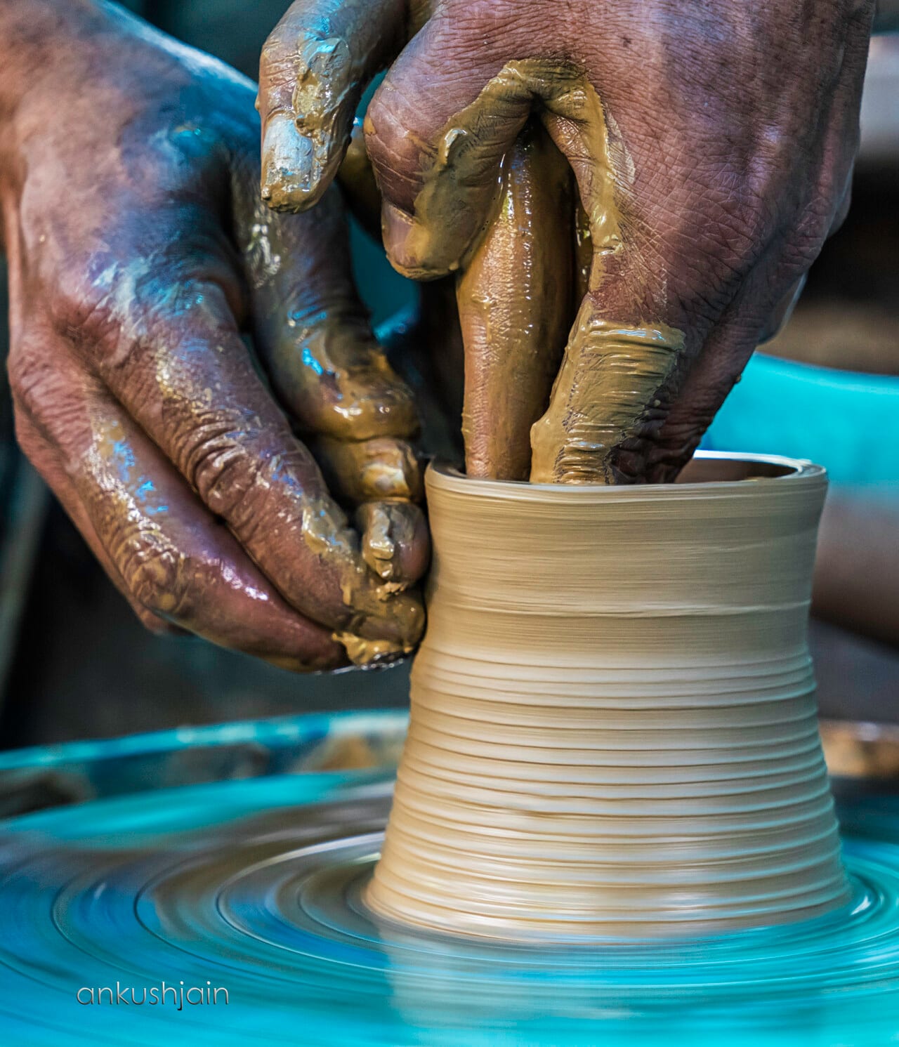 Potter's clay-stained hands shaping a tall pot on the wheel, Sobha Singh Art Gallery, Palampur