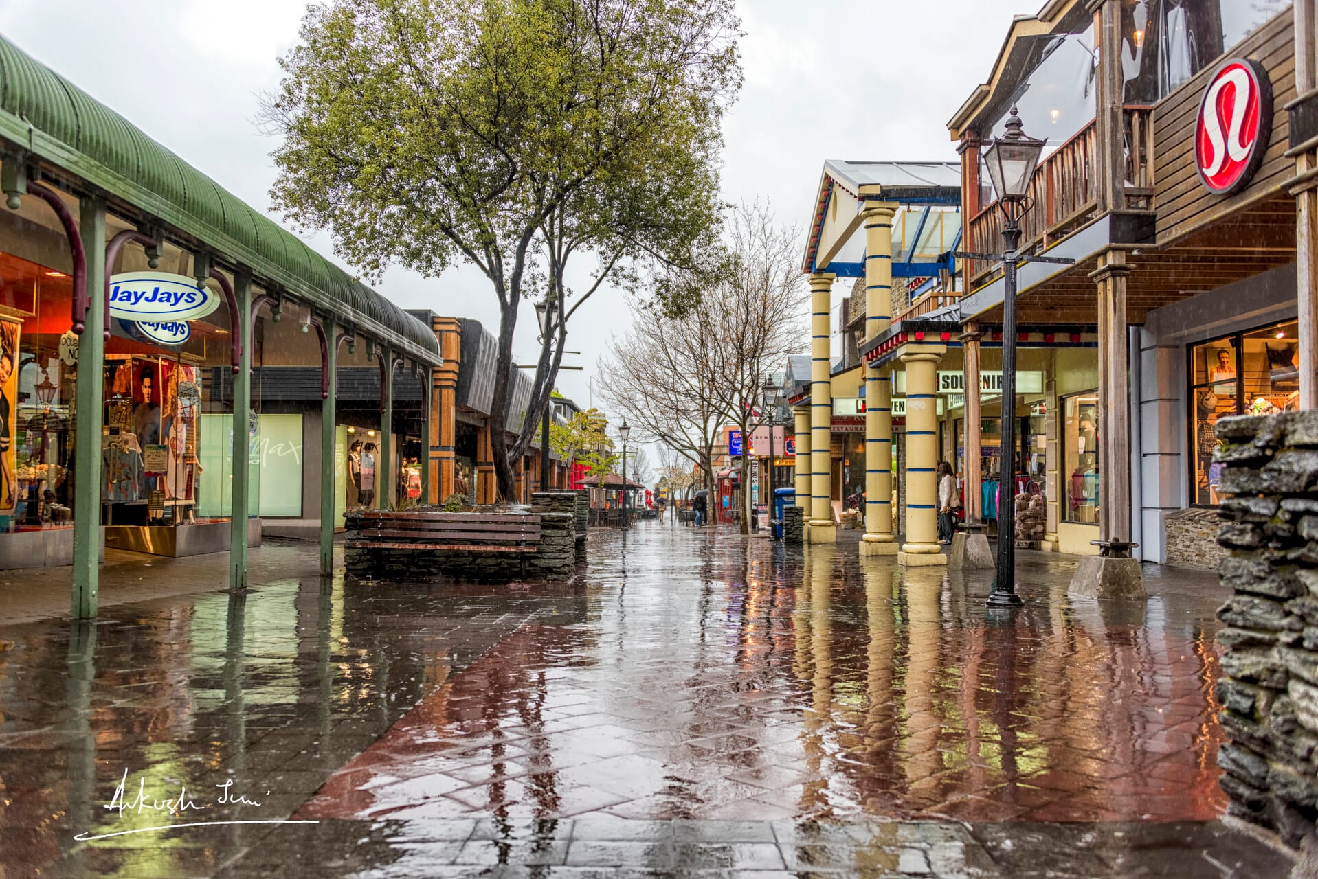 Wet cobblestone street reflecting shopfronts after rain, Queenstown