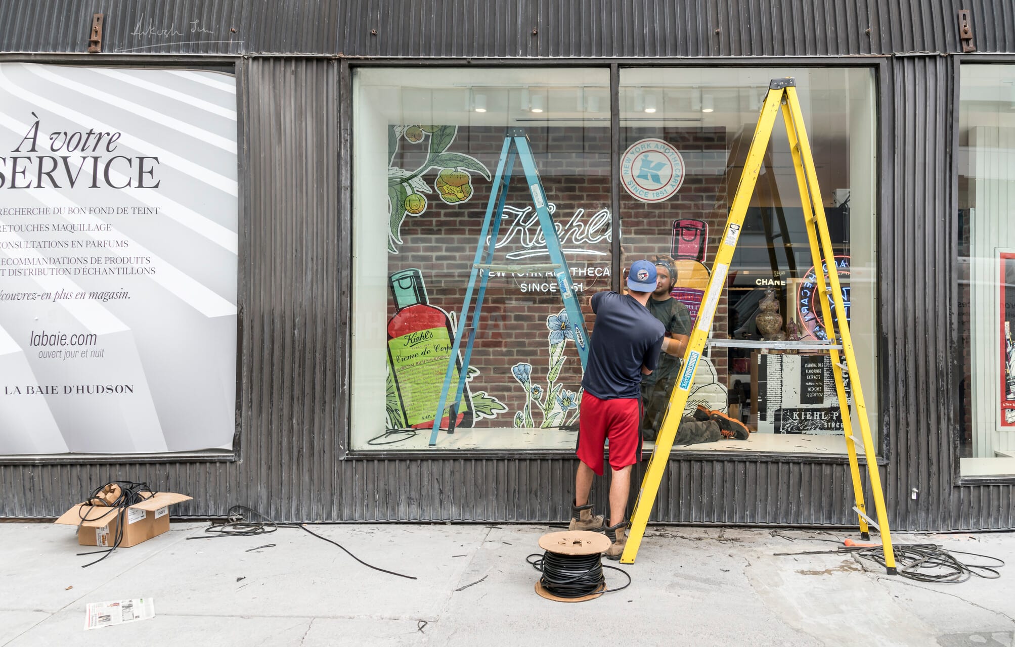 Window dresser on a tall ladder fitting out a shopfront in Montreal