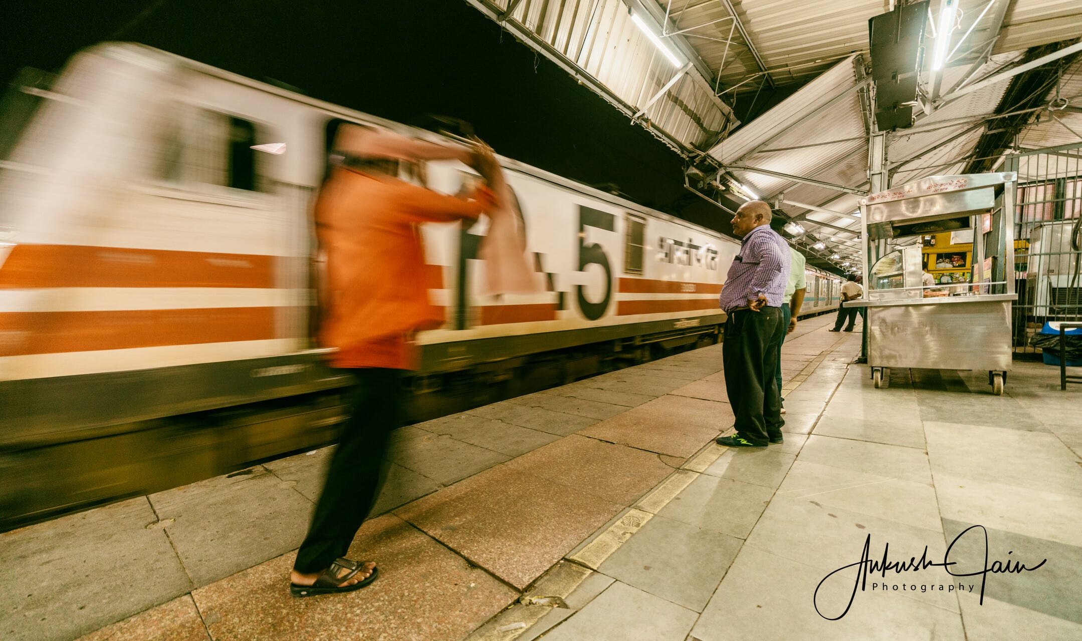 Motion-blurred train pulling in as a passenger waves from the platform, Ludhiana Junction