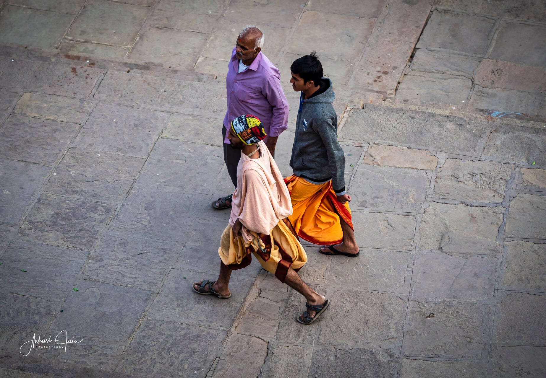 Sadhu in a saffron dhoti walking the stone flagstones beside two passersby, Varanasi