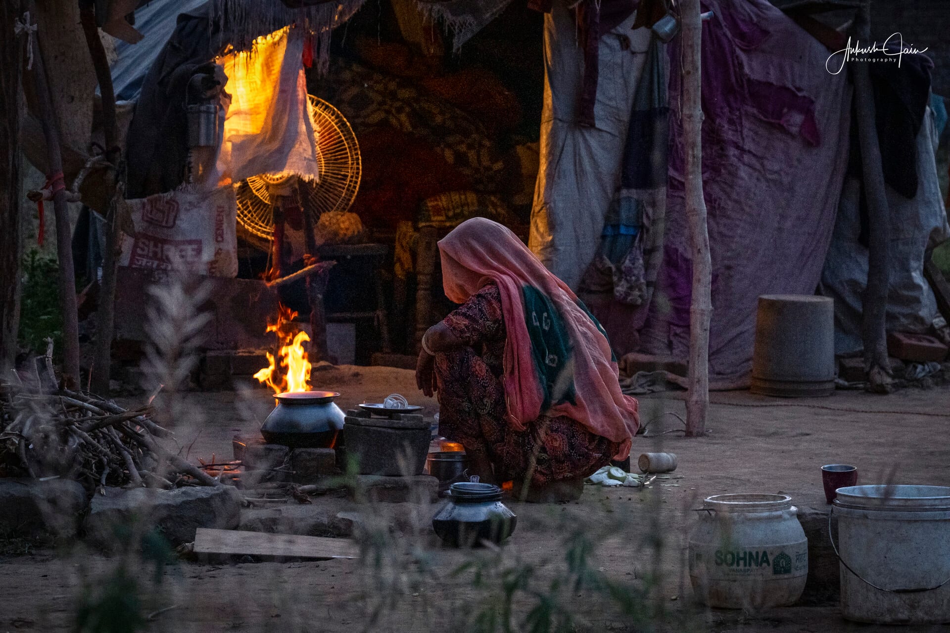 Woman beside a wood fire at dusk at a Gujjar camp, Mahaveer Enclave, Barewal