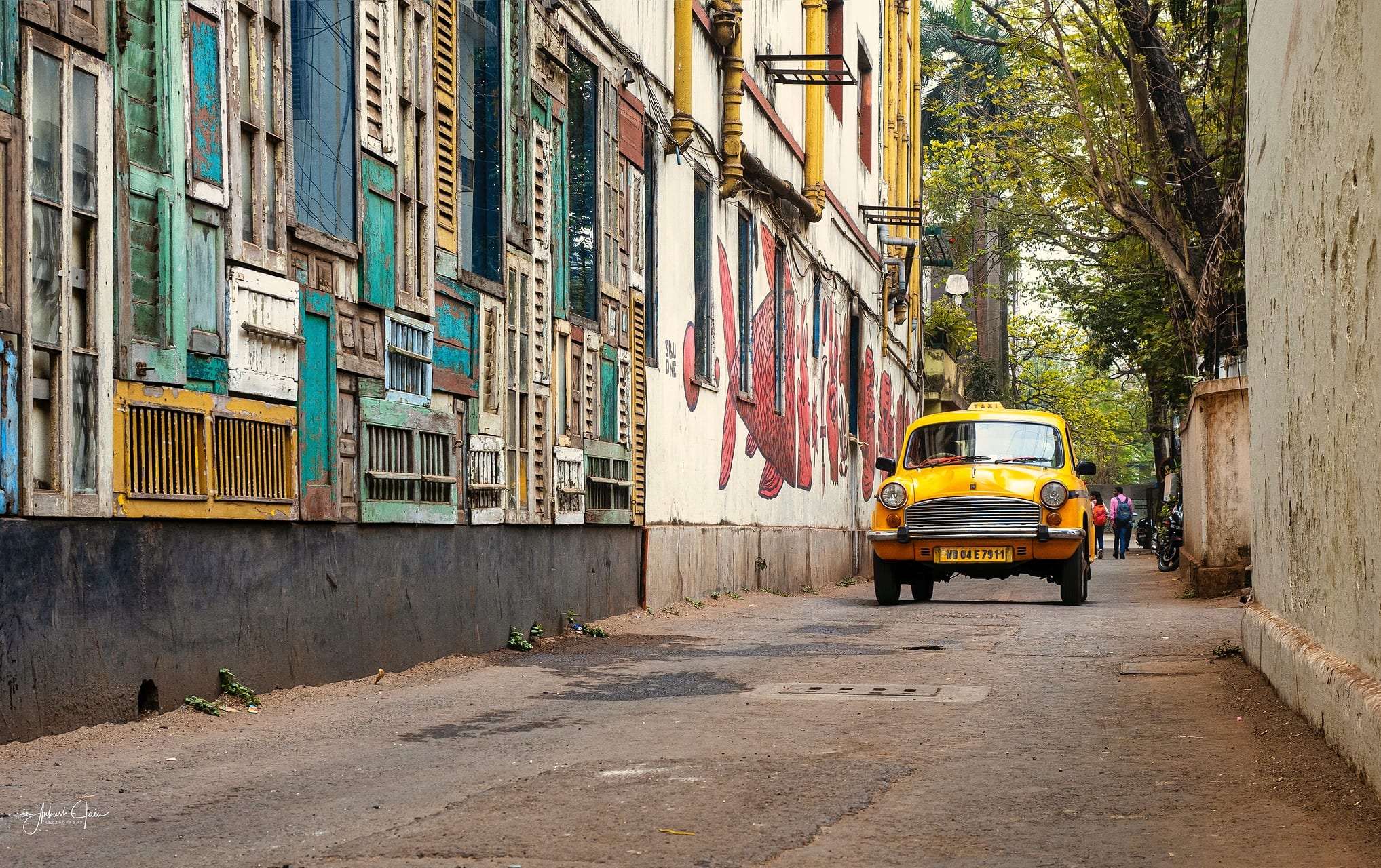Yellow Ambassador taxi on an arty cafe lane in Kolkata, painted shutters lining the street