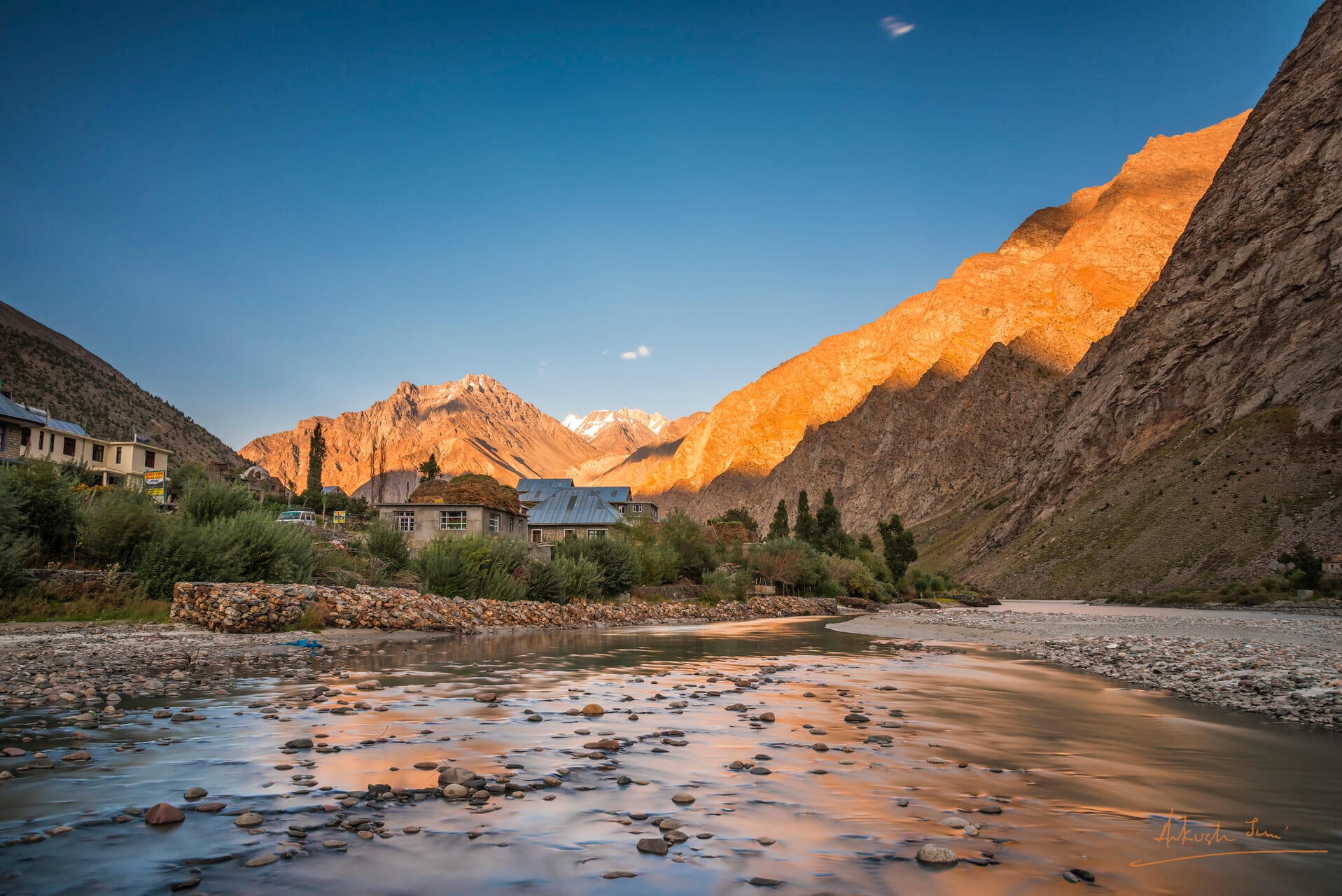 Long-exposure of the Bhaga river running past stone village houses in Jispa, golden light on the cliff above