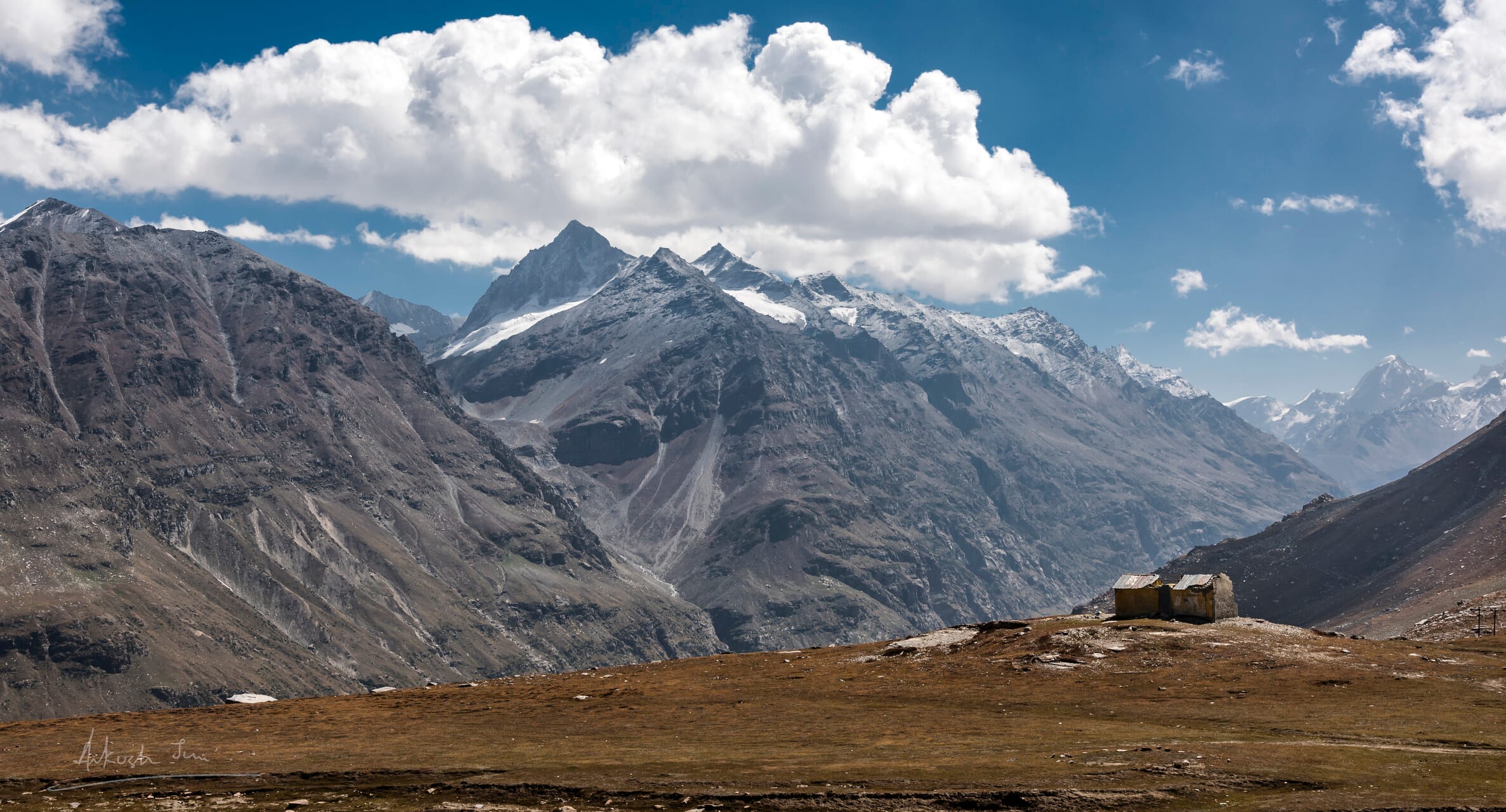 Lone stone hut on a high pass near Baralacha, snow peaks rolling behind
