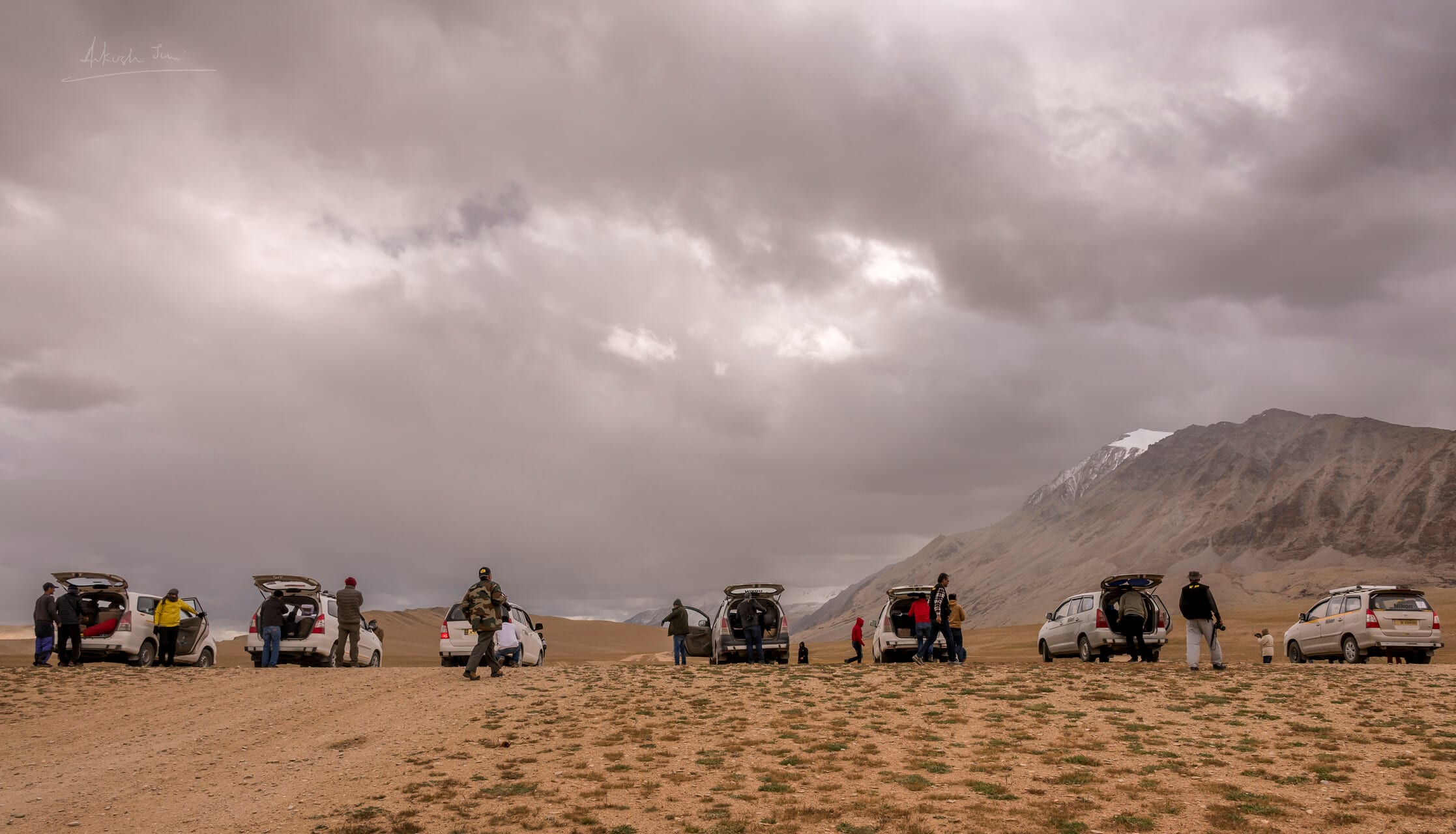 A caravan of cars and travellers stopped on the wide Tso Kar plains, snow peak in the distance