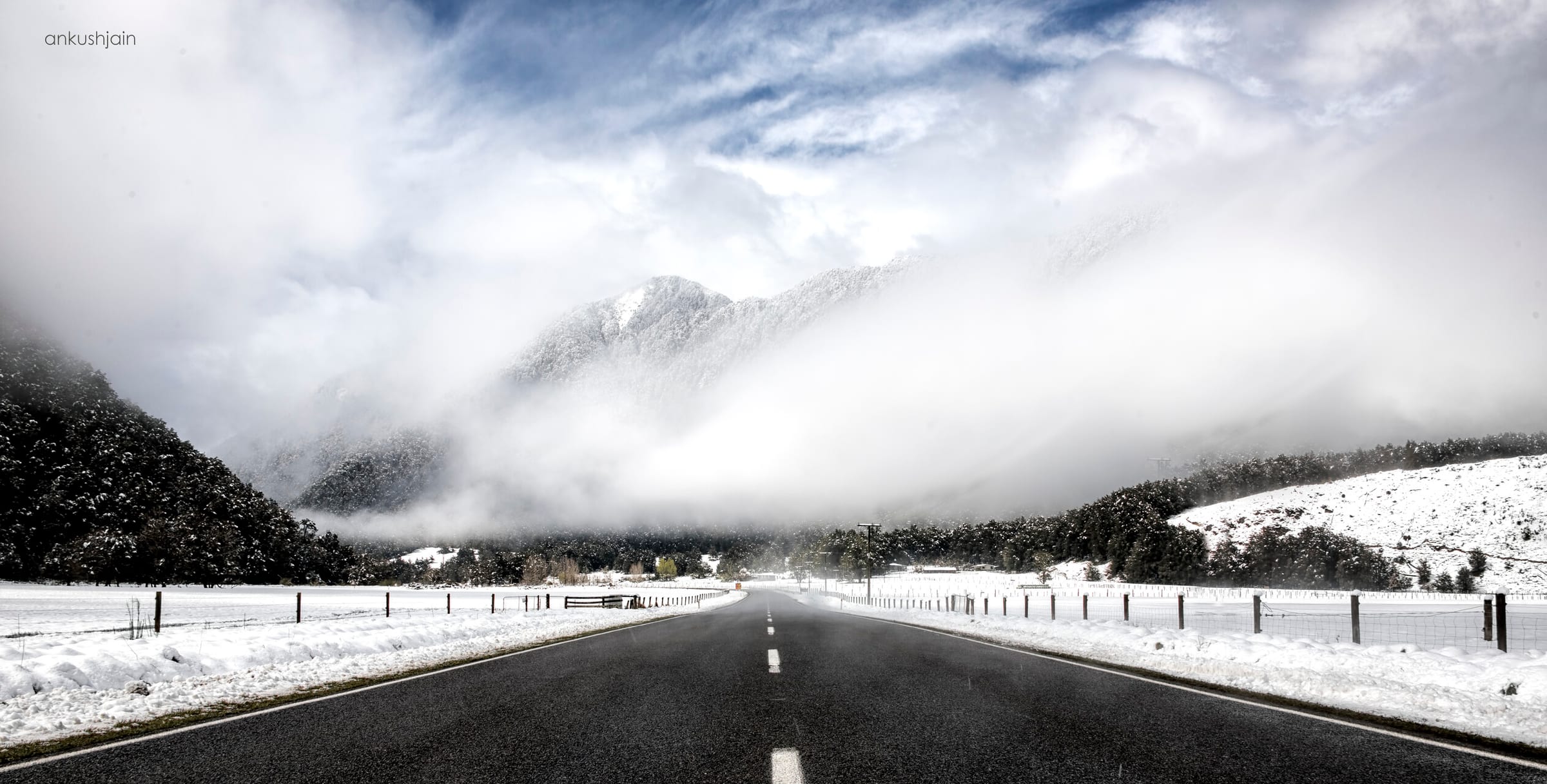 Empty highway leading into a cloud-wreathed snowy valley, alpine route from Kaikoura to Queenstown