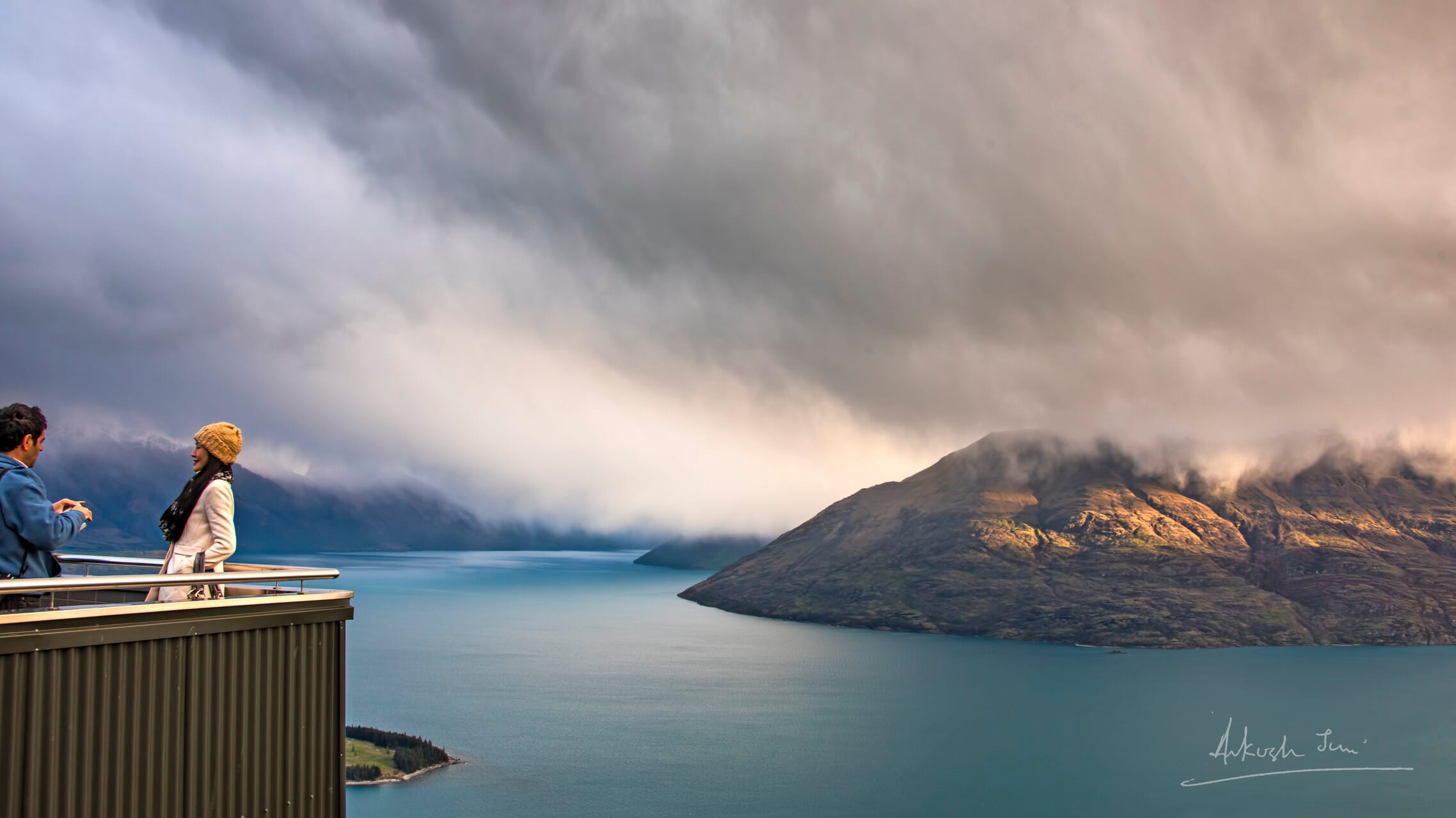 Two travellers on the Skyline viewing platform above Lake Wakatipu under heavy storm clouds, Queenstown