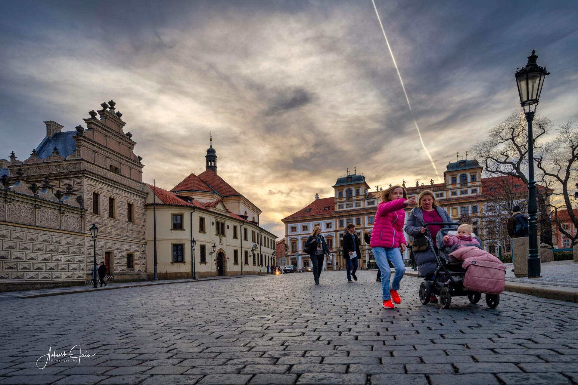 A family crossing a cobblestone Prague square at sunset