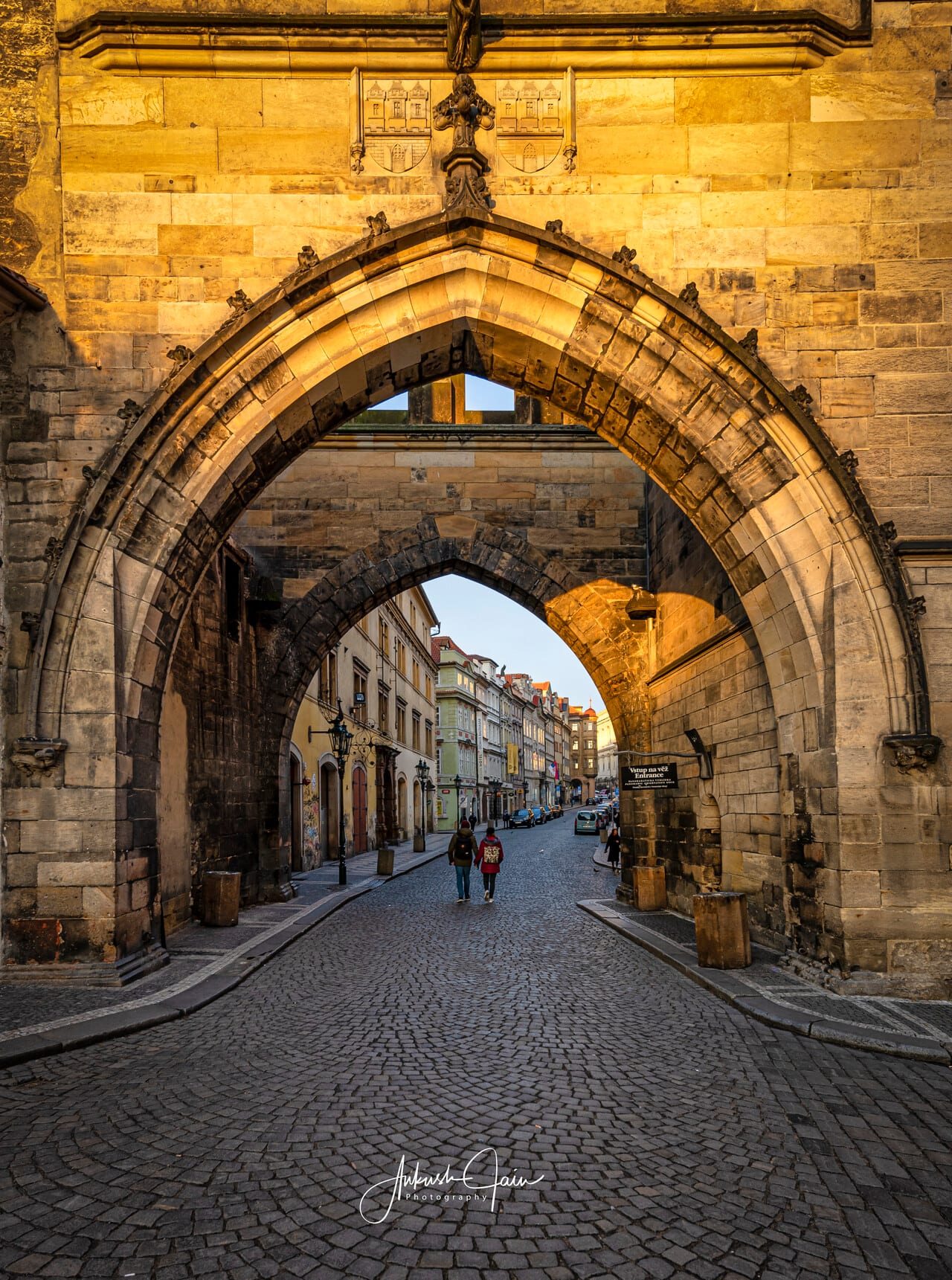Lesser Town Bridge Tower archway opening onto Mostecká street, one figure walking through in golden light