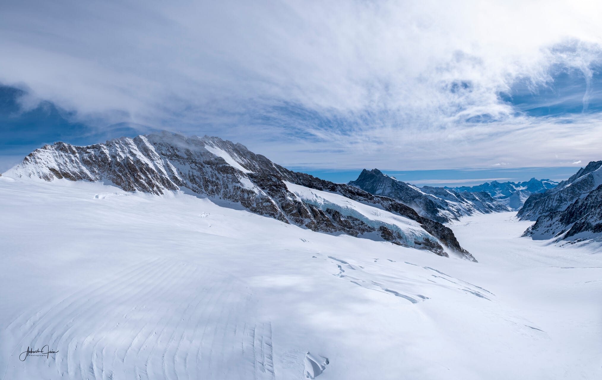 View from Jungfraujoch over the Aletsch glacier — a vast snowfield curving away under thin streaks of high cloud