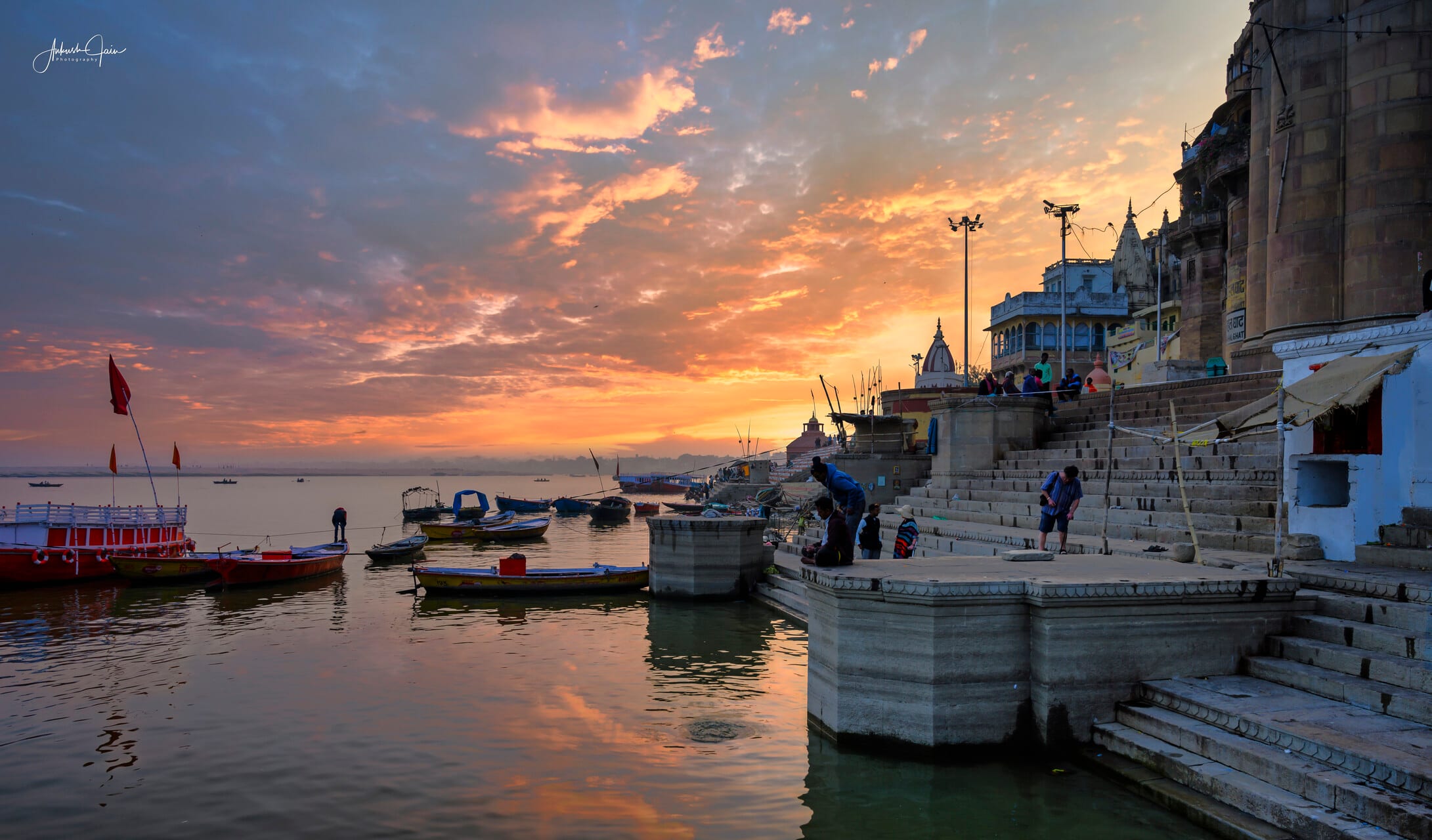 Boats moored at Guleria Ghat at sunrise, orange clouds spreading over the Ganga