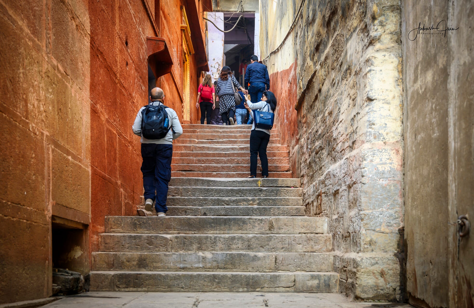 Travellers climbing stone stairs in the ochre-walled street by Guleria Kothi, Varanasi