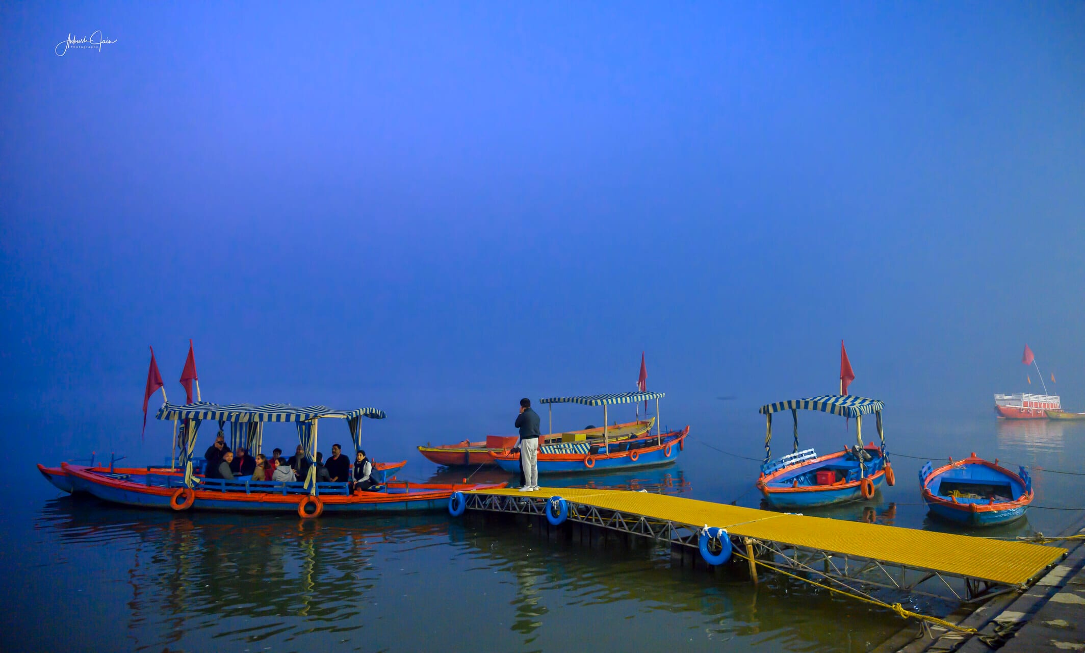 Misty winter dawn at Guleria Ghat, red-flagged boats moored to a yellow walkway